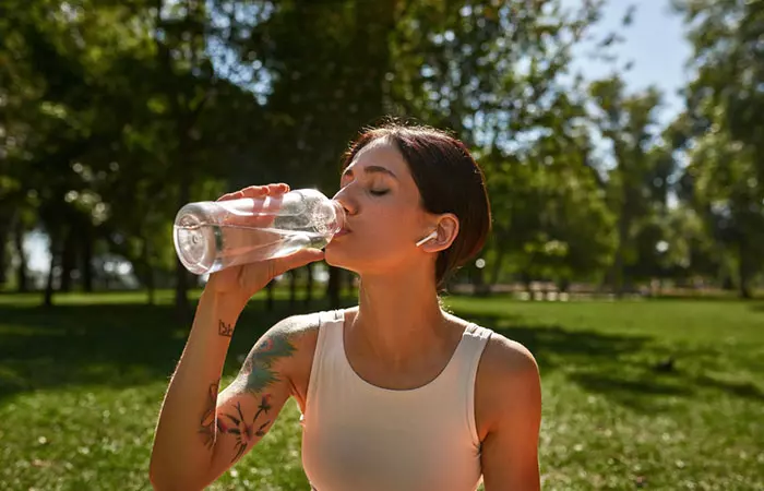 A woman with a tattoo drinks water to hydrate herself