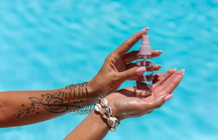 A woman with an arm tattoo carrying vitamin E oil in a spray bottle at the pool