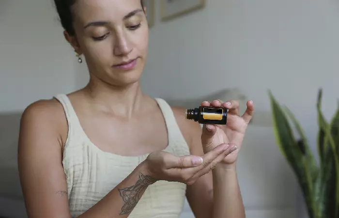 A woman with an arm tattoo pouring vitamin E oil into her palm