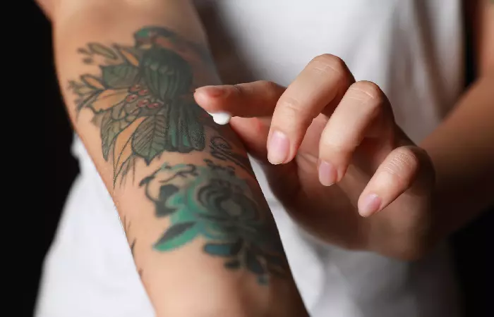 A woman with colored tattoos on her arm applying moisturizer
