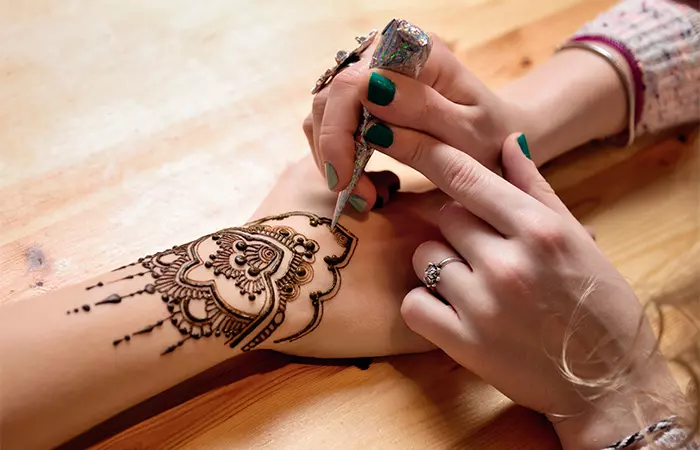An artist applying henna tattoo on the back of a woman’s hand