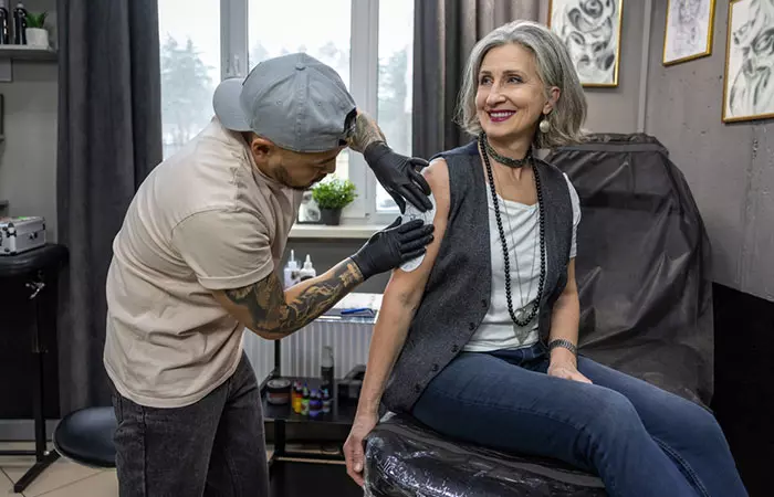 An elderly woman getting a tattoo on her shoulder
