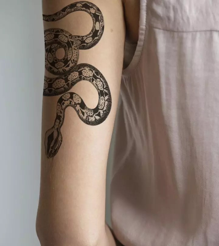 An intricate snake tattoo in black ink on the upper arm of a woman