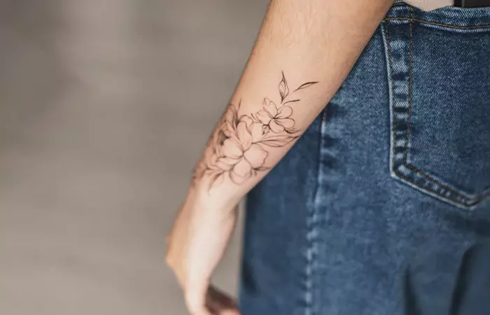 Close up of a floral fine line tattoo on a woman’s forearm