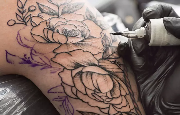 An artist tattooing botanical flower designs on a woman