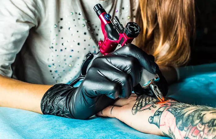 A tattoo artist covering up a black tattoo with color