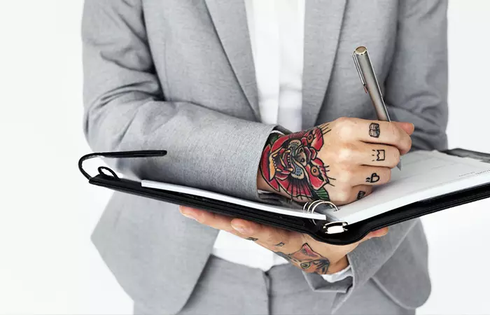 Close-up of a lawyer with tattoos holding a pen and a notebook
