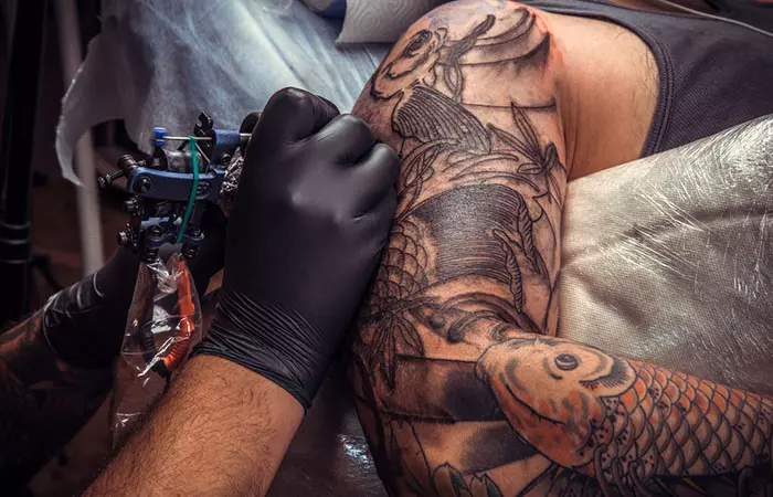 A tattoo artist inks on the upper arm of a client during a tattoo cover-up session