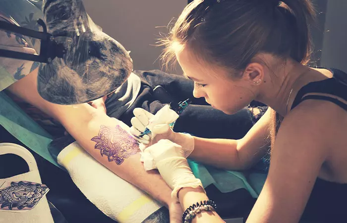 A female tattoo artist drawing a tattoo on her client’s arm