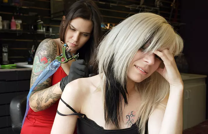 A woman experiencing pain while getting a tattoo on her back