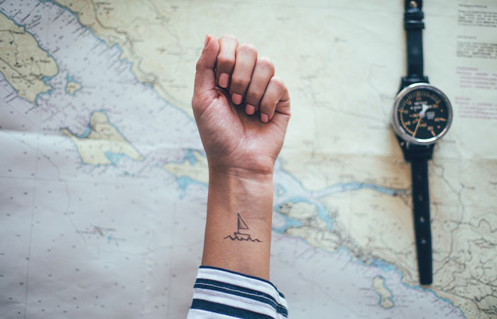 A close up of a female wrist with a simple boat line tattoo