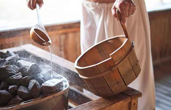 A man pouring water on the rocks to produce steam in the sauna