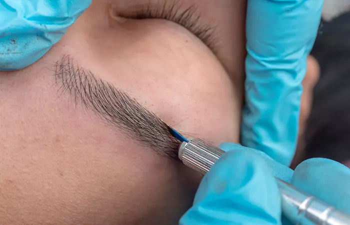An aesthetician microblading a woman’s eyebrow