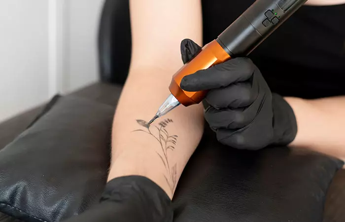 Woman tattooing her arm