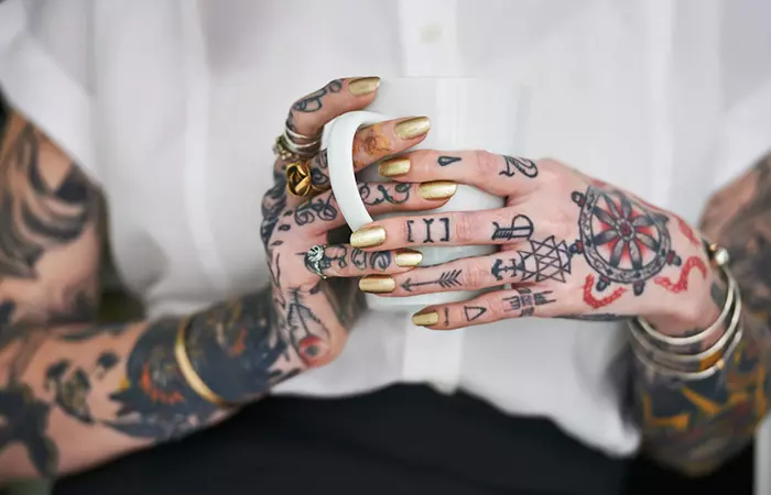 Woman with multiple hand and finger tattoos holding a white cup
