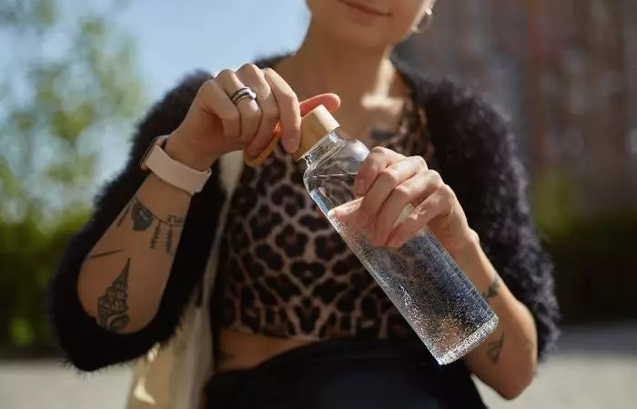 Woman with tattoos holding a water bottle of water to hydrate herself