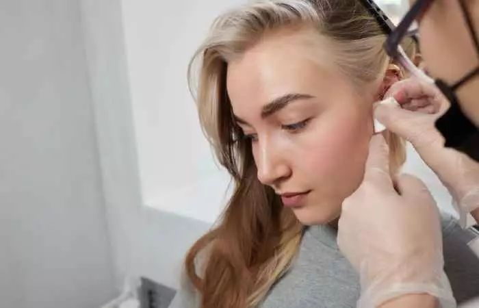 A piercing artist applying a solution to a woman’s forward helix piercing