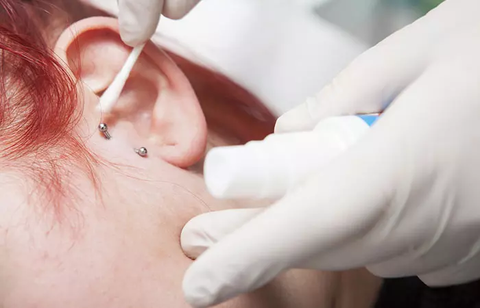 A professional piercer cleans a client’s ear piercing and the surrounding area