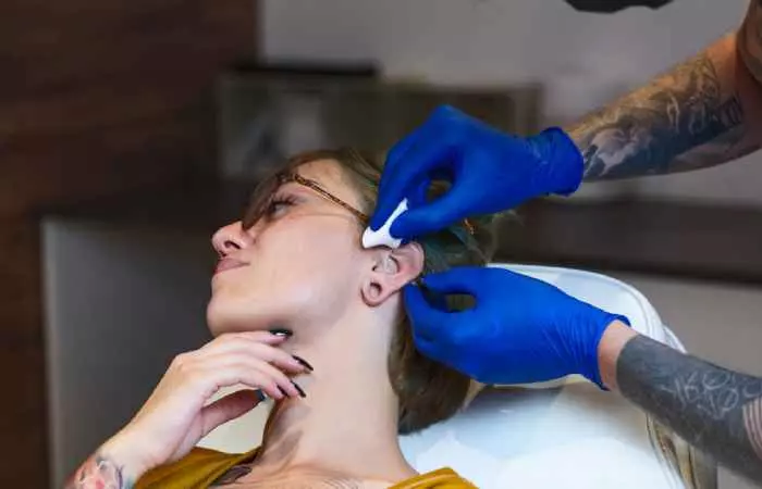 A tattoo artist prepares a client for daith piercing on her left ear