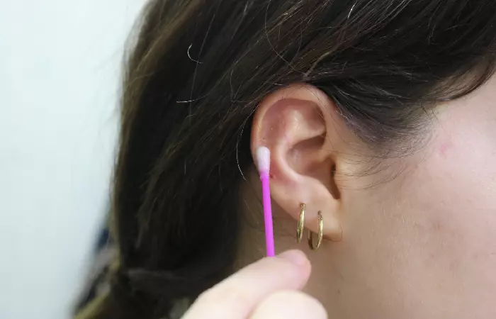A woman applying healing ointment to her cartilage piercing bump using a Q-tip