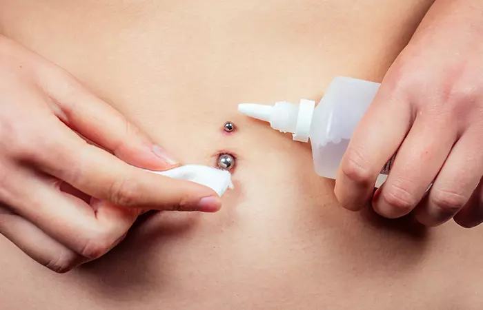 A woman cleaning the pierced navel area with a sterile solution