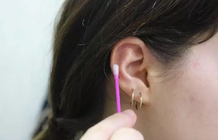 A woman cleans an ear piercing and the surrounding area with a cotton swab