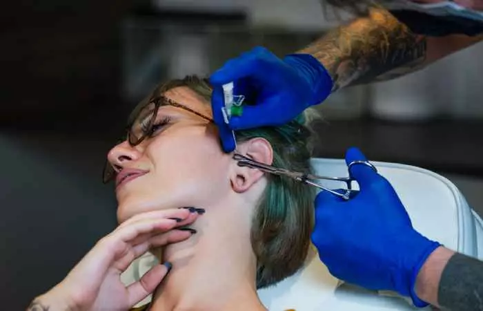 A woman getting her tragus pierced