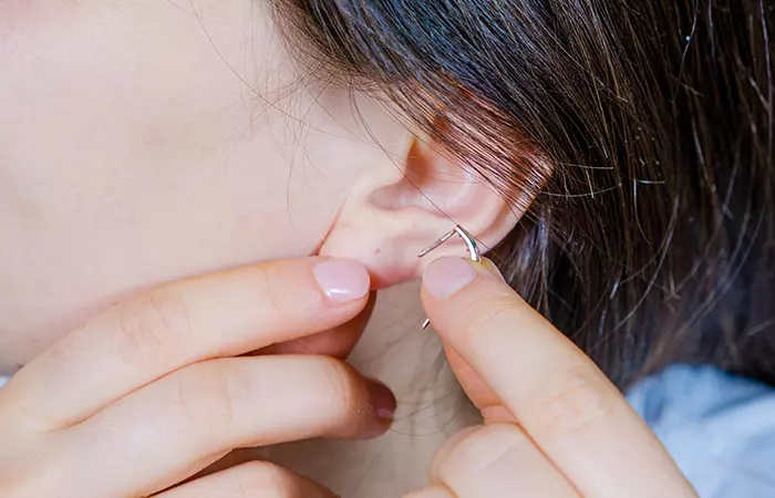 A woman trying to re-open her closed ear piercing at home