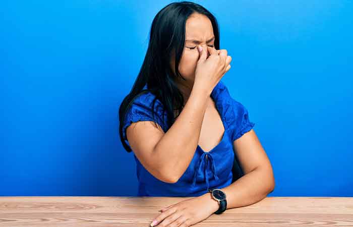 A woman holds the bridge of her nose in pain