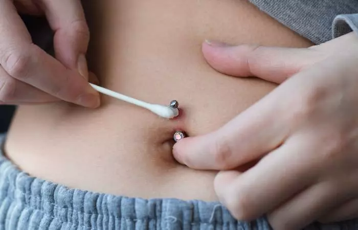 A woman cleaning her belly button piercing with a Q-tip