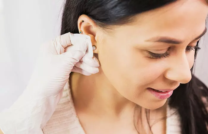 Doctor in sterile gloves preparing a woman's ear for a piercing procedure