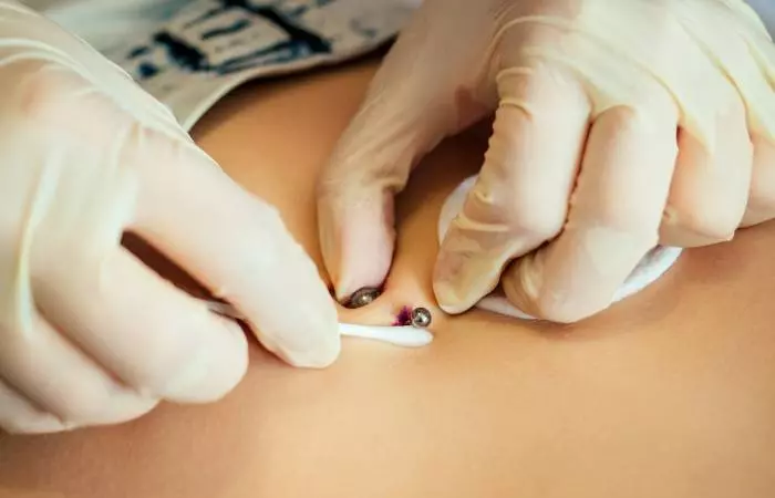 A piercer doing a navel piercing