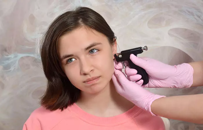 A young girl in pain as she gets her ear lobe pierced with a piercing gun