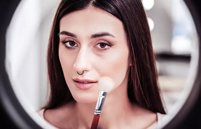 Woman applying makeup near her nose piercing