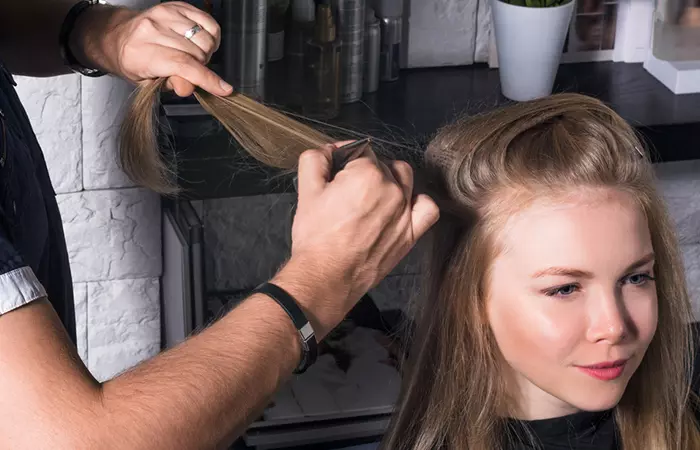 A hairstylist using a rat-tail comb to tease a woman’s hair and build volume