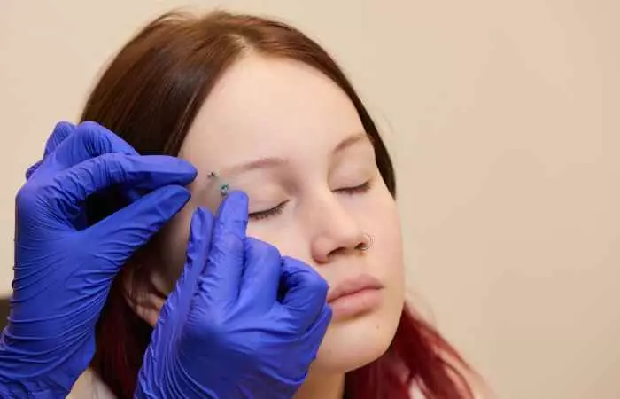 A piercer adjusting the eyebrow piercing of the client.