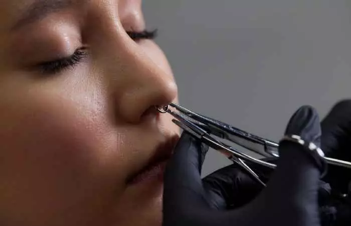 A piercer working on her client’s nose piercing