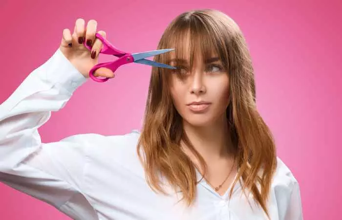A woman holding hair shears to her hair