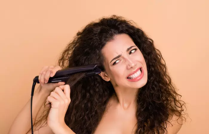 A woman struggling to straighten her natural hair with a ceramic hair straightener
