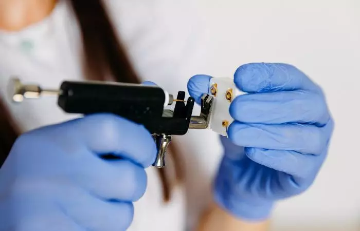 A piercer inserting gold earrings into a piercing gun