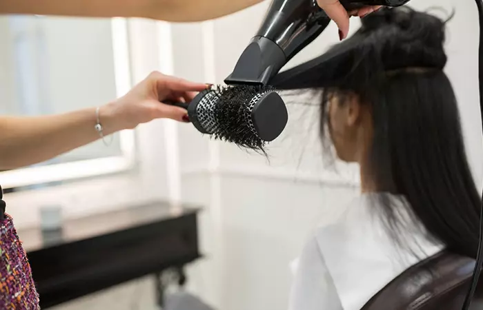 Hairdresser drying woman's hair with hair dryer and round brush in a beauty salon