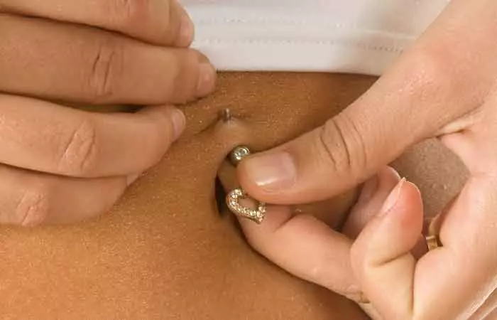 Woman removing belly button piercing jewelry to clean it