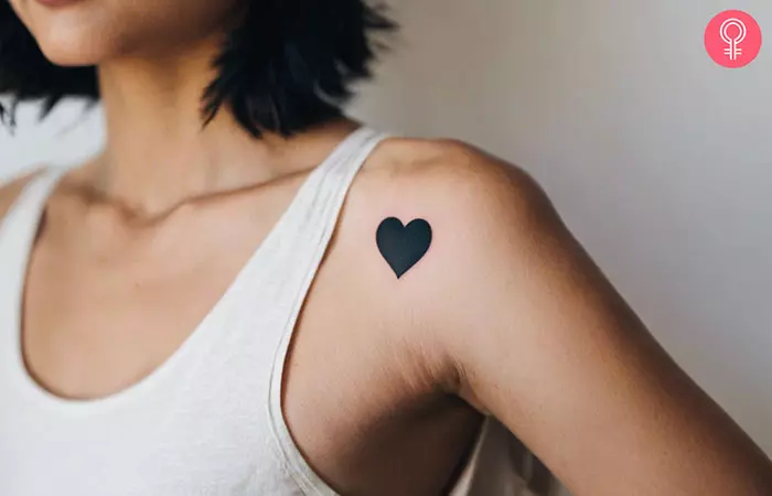 Woman with a minimalistic black heart tattoo on her shoulder