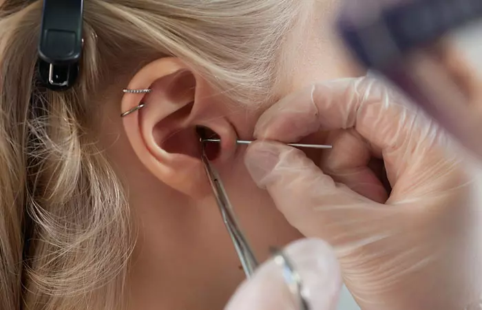 A piercer using a needle to create a tragus piercing