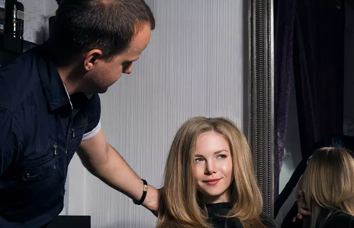 hairstylist smoothing the top layer of teased hair for final look