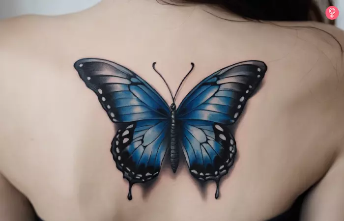 Blue and black butterfly tattoo on a woman’s back