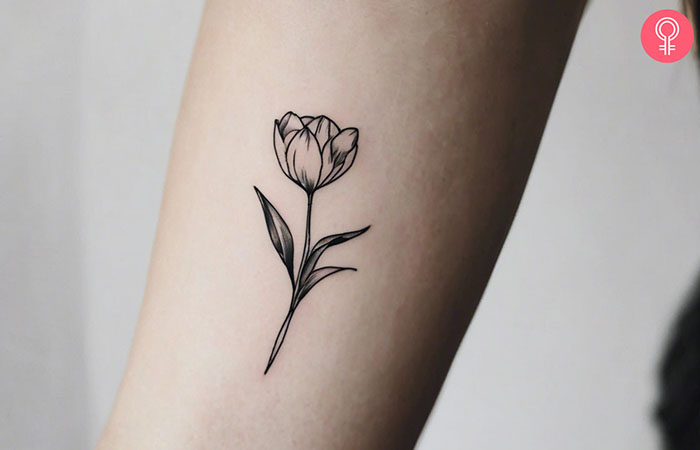 A fine line tulip tattoo on the upper arm