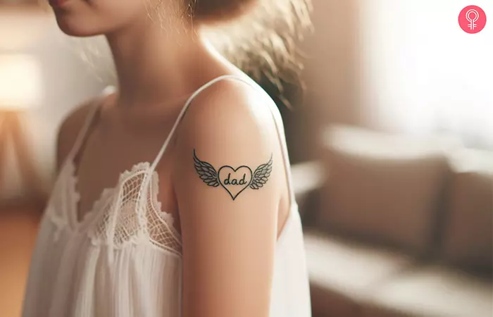 A memorial heart with wings tattoo on the upper arm of a woman