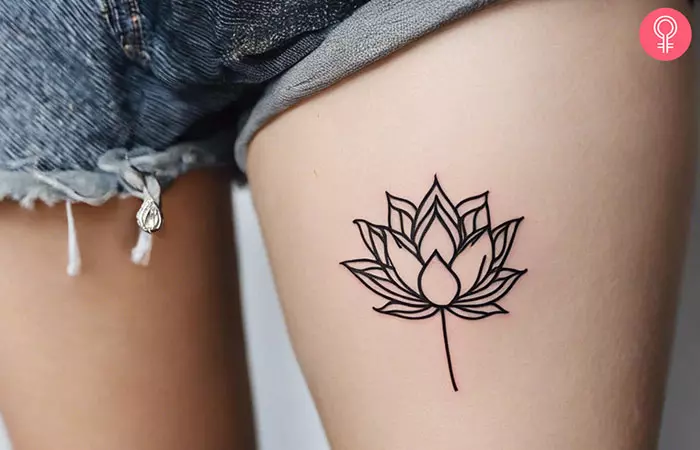 A tattoo of a simple lotus in black ink on the upper thigh