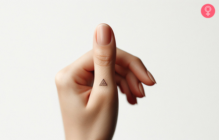 A tiny triangle tattoo on the thumb